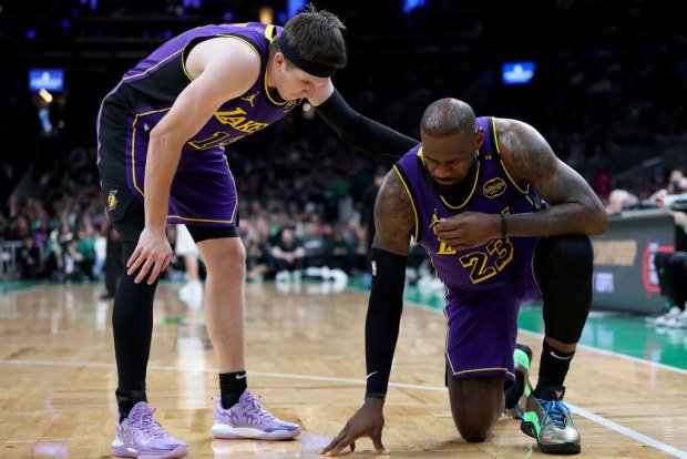 Austin Reaves #15 of the Los Angeles Lakers checks on teammate LeBron James #23 after James collided with Jayson Tatum #0 of the Boston Celtics.